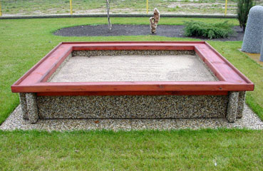 Betonowa piaskownica z wygodnym siedzikiem wykonanym z drewna iglastego zbezpiczonym powierzchniowo lakierem.